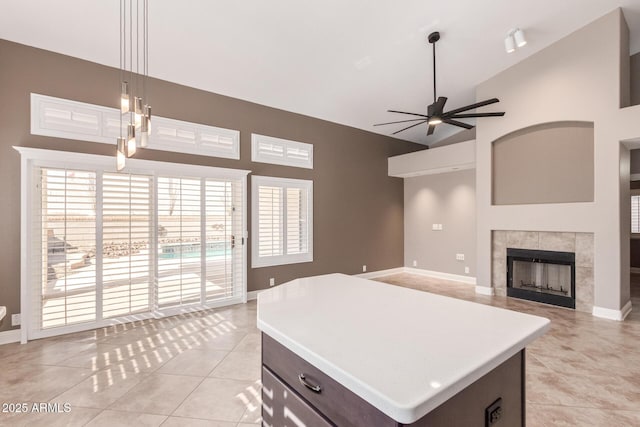 kitchen with high vaulted ceiling, a ceiling fan, light tile patterned flooring, light countertops, and a tile fireplace