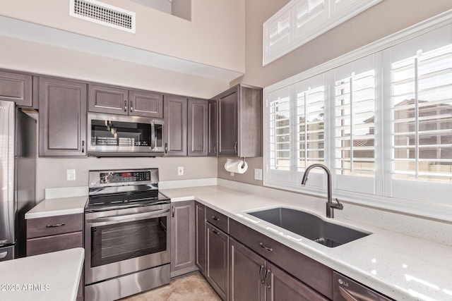 kitchen featuring dark brown cabinets, visible vents, appliances with stainless steel finishes, light countertops, and a sink