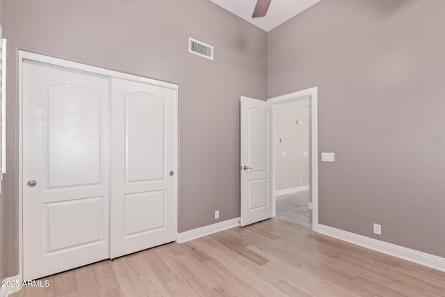 unfurnished bedroom with visible vents, a closet, baseboards, a towering ceiling, and light wood-style flooring