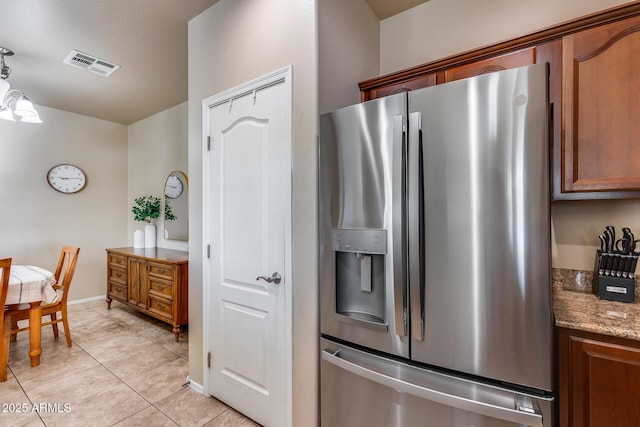 kitchen with light tile patterned floors, visible vents, baseboards, stone counters, and stainless steel refrigerator with ice dispenser