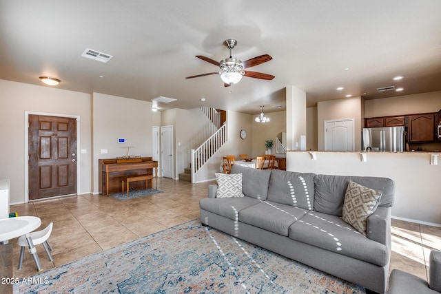 living area with light tile patterned floors, stairs, visible vents, and ceiling fan with notable chandelier