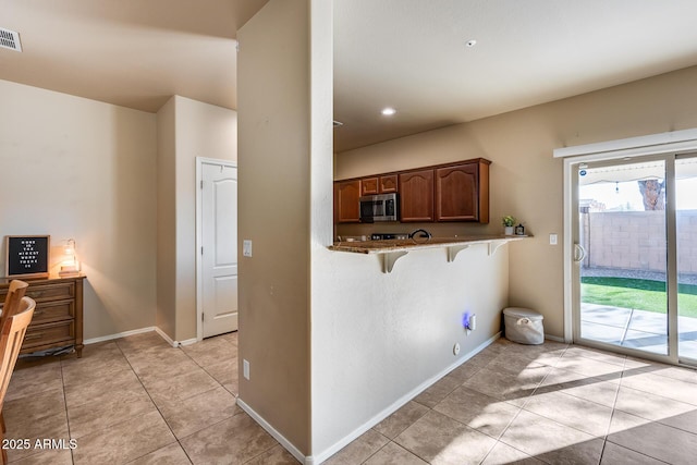 kitchen featuring a kitchen bar, stainless steel microwave, visible vents, light tile patterned flooring, and baseboards