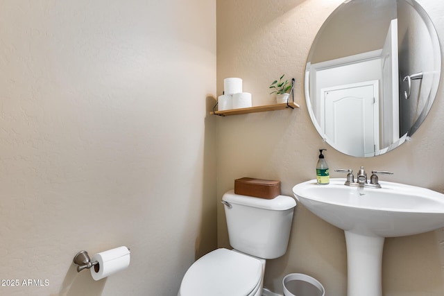 half bath with a textured wall, a sink, and toilet