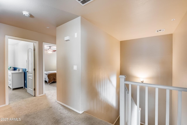 corridor with light colored carpet, visible vents, and baseboards