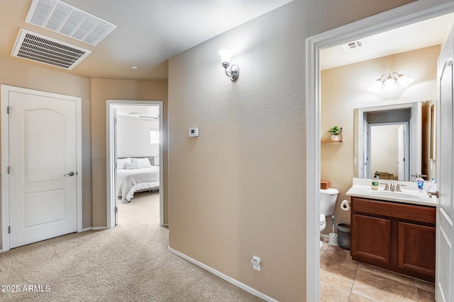 hall with light carpet, a sink, visible vents, and baseboards