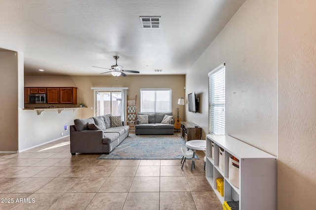 living area with visible vents, ceiling fan, baseboards, and light tile patterned floors