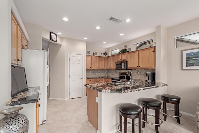 kitchen with visible vents, a peninsula, decorative backsplash, appliances with stainless steel finishes, and a kitchen breakfast bar