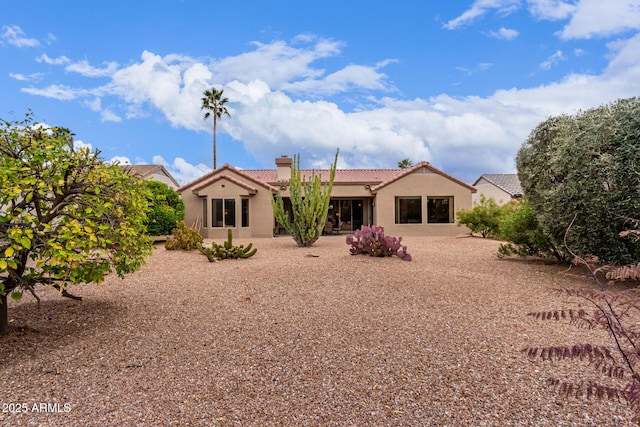 rear view of property featuring stucco siding, a patio area, a chimney, and a tiled roof