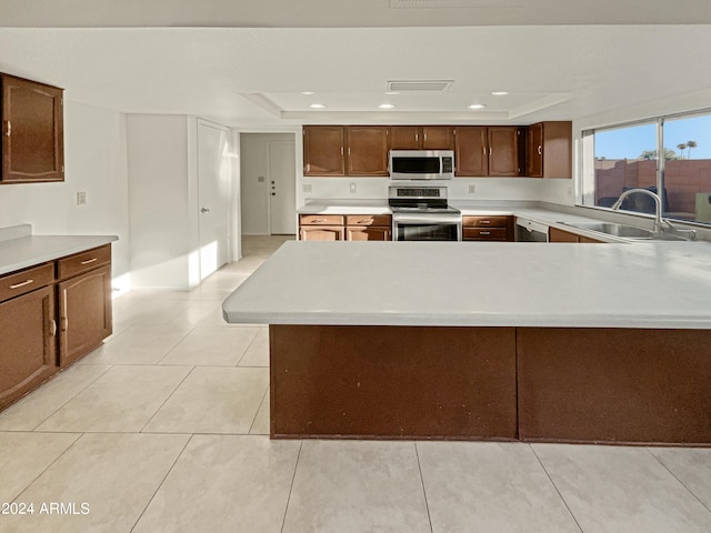 kitchen featuring appliances with stainless steel finishes, a tray ceiling, sink, and light tile patterned floors