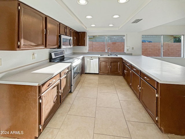 kitchen featuring appliances with stainless steel finishes, a raised ceiling, kitchen peninsula, light tile patterned floors, and sink