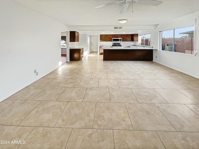 unfurnished living room featuring ceiling fan, sink, light tile patterned floors, and a textured ceiling