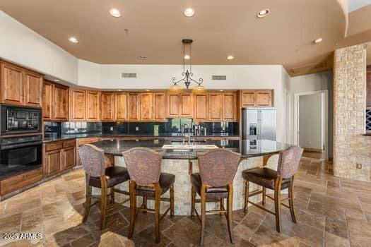 11986 N 134th Pl, Scottsdale, AZ 85259 - kitchen with black appliances, brown cabinetry, dark countertops, a center island with sink, and recessed lighting