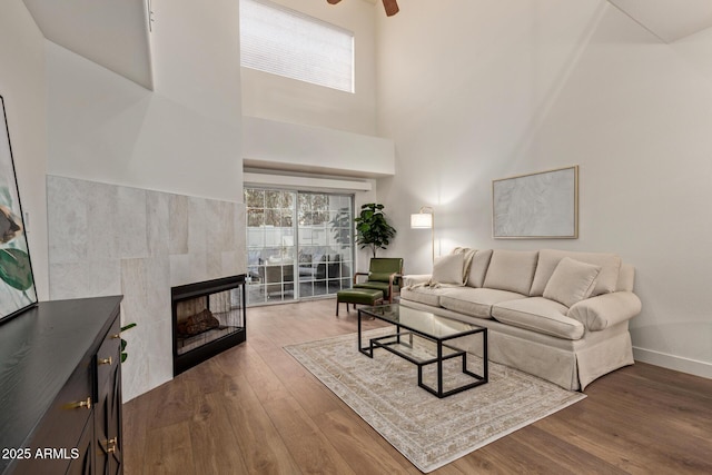 7710 E Gainey Ranch Rd Unit 142, Scottsdale, AZ 85258 - living room featuring wood finished floors, a tile fireplace, healthy amount of natural light, a towering ceiling, and ceiling fan