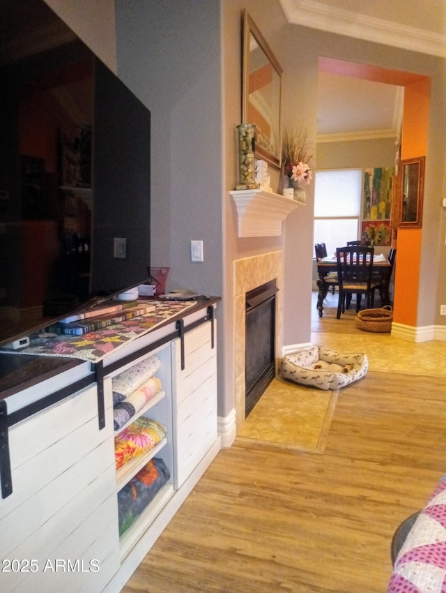 interior space featuring a tiled fireplace, wood finished floors, baseboards, and ornamental molding