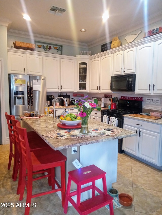 kitchen with visible vents, a breakfast bar area, ornamental molding, light tile patterned floors, and stainless steel appliances