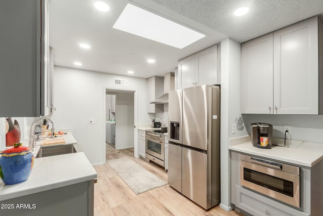 kitchen with sink, light hardwood / wood-style flooring, light stone countertops, appliances with stainless steel finishes, and wall chimney exhaust hood