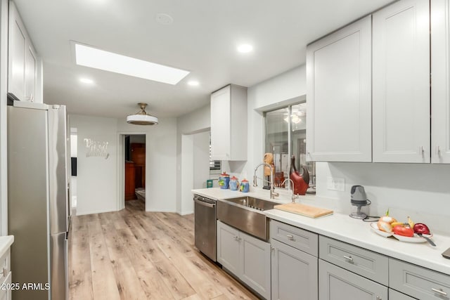 kitchen with light hardwood / wood-style floors, sink, a skylight, appliances with stainless steel finishes, and gray cabinetry