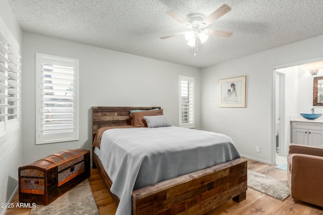 bedroom with ceiling fan, a textured ceiling, ensuite bathroom, and light wood-type flooring