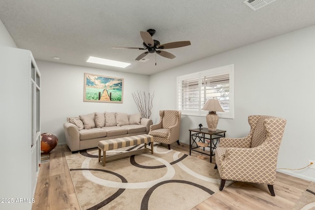 living room featuring ceiling fan, a textured ceiling, a skylight, and light wood-type flooring