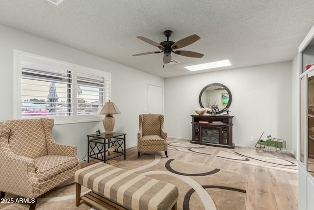 sitting room with wood-type flooring, a textured ceiling, ceiling fan, and a fireplace