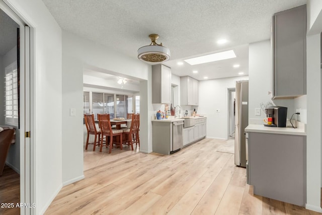 kitchen with light hardwood / wood-style floors, a skylight, appliances with stainless steel finishes, gray cabinetry, and a textured ceiling