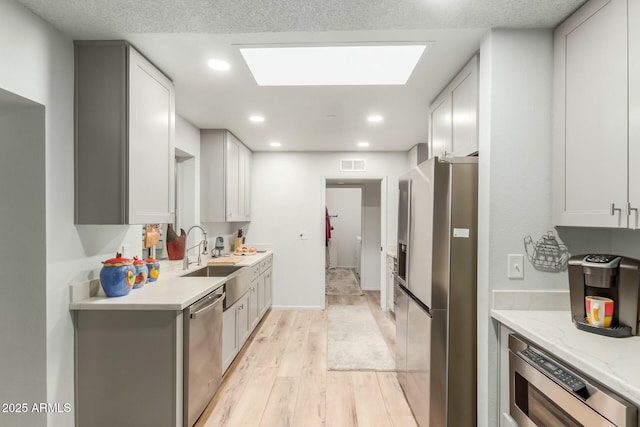 kitchen with light stone countertops, white cabinetry, stainless steel appliances, sink, and light wood-type flooring