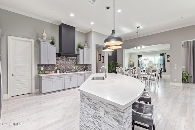 kitchen with pendant lighting, wall chimney range hood, sink, gray cabinetry, and stainless steel gas stovetop