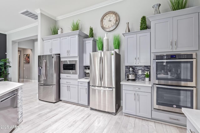 kitchen with tasteful backsplash, ornamental molding, stainless steel appliances, and light wood-type flooring