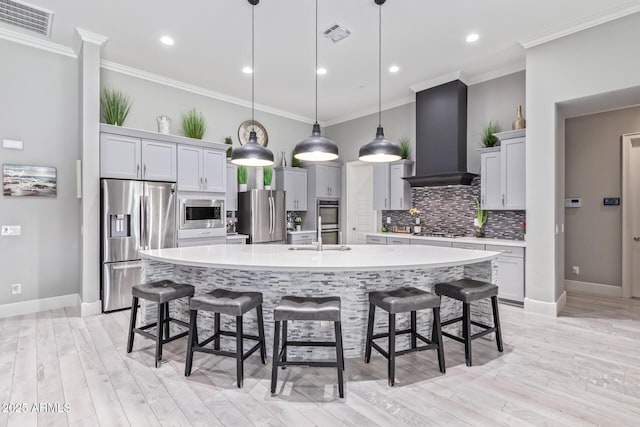 kitchen with a kitchen bar, custom exhaust hood, hanging light fixtures, a large island with sink, and stainless steel appliances