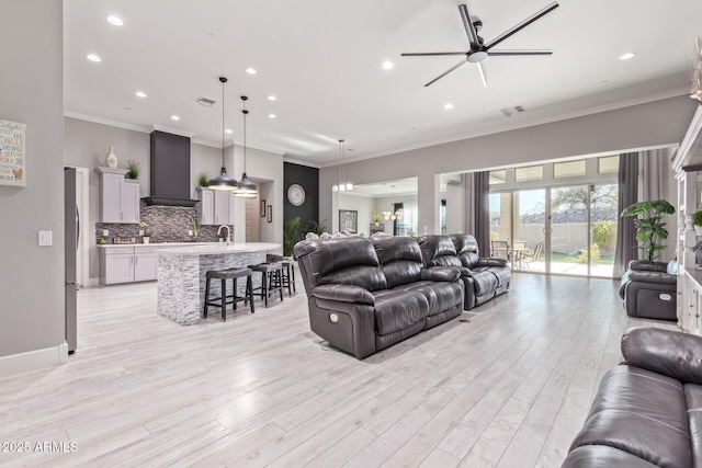 living room with ceiling fan, ornamental molding, sink, and light wood-type flooring