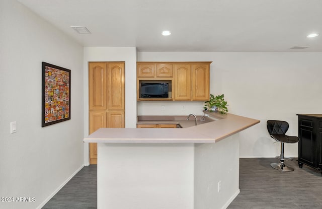 kitchen featuring black microwave, dark hardwood / wood-style floors, kitchen peninsula, a breakfast bar area, and light brown cabinetry