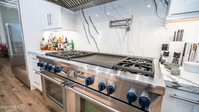 kitchen featuring white cabinetry, light stone countertops, premium appliances, and light hardwood / wood-style flooring