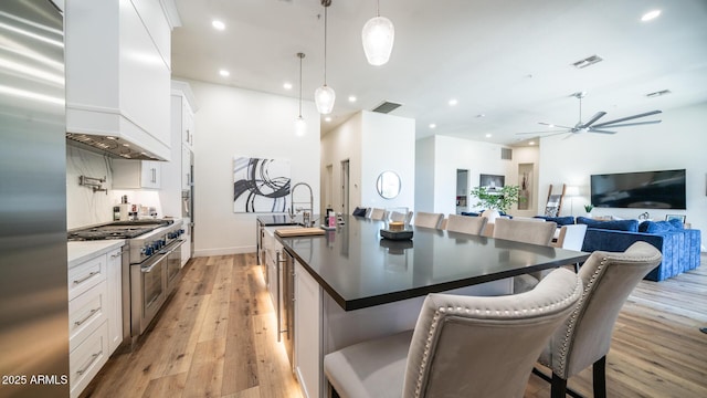 kitchen featuring a breakfast bar, appliances with stainless steel finishes, custom range hood, white cabinets, and decorative light fixtures