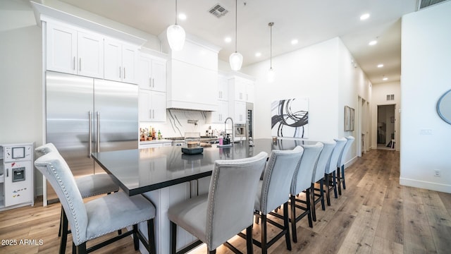 kitchen with white cabinetry, hanging light fixtures, a kitchen island with sink, and built in fridge