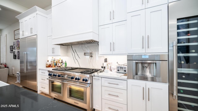 kitchen featuring high quality appliances, custom range hood, white cabinets, beverage cooler, and backsplash