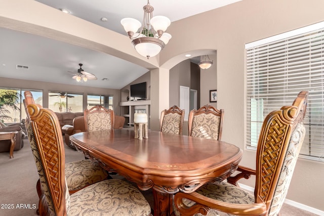 dining room with ceiling fan with notable chandelier, light colored carpet, built in features, and vaulted ceiling