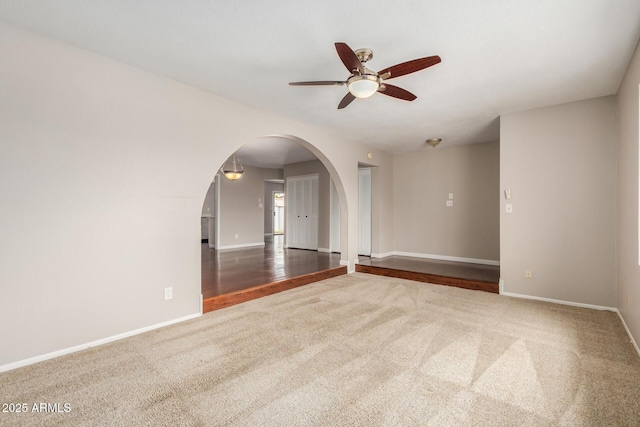 carpeted empty room featuring arched walkways, a ceiling fan, and baseboards