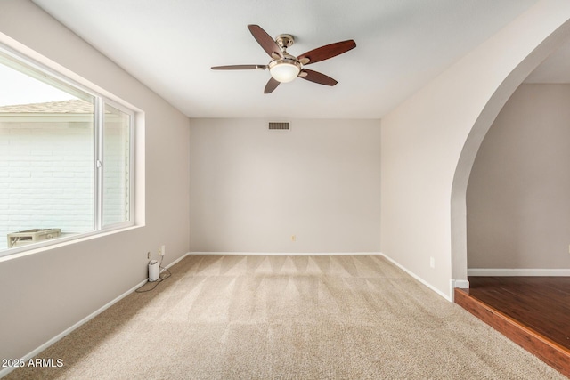 carpeted spare room featuring arched walkways, healthy amount of natural light, ceiling fan, and baseboards
