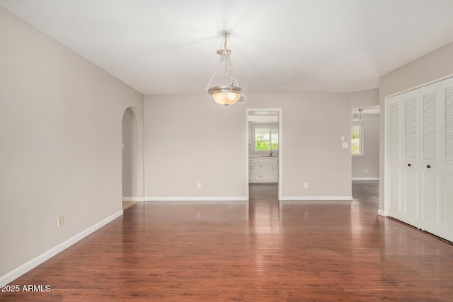 unfurnished living room featuring arched walkways, baseboards, and wood finished floors