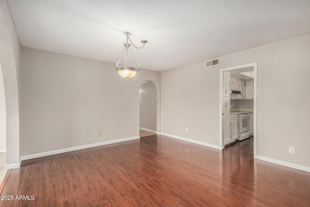 empty room featuring arched walkways, dark wood-style flooring, and baseboards
