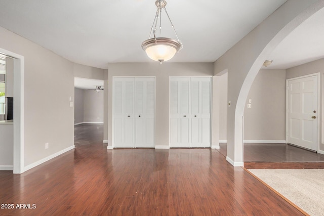 entrance foyer with arched walkways, dark wood finished floors, and baseboards