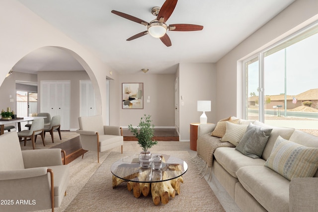 living area with arched walkways, plenty of natural light, a ceiling fan, and carpet floors