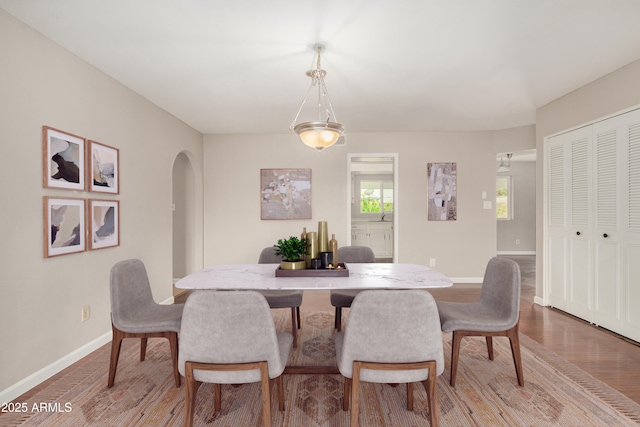 dining area with light wood-style floors, arched walkways, and baseboards