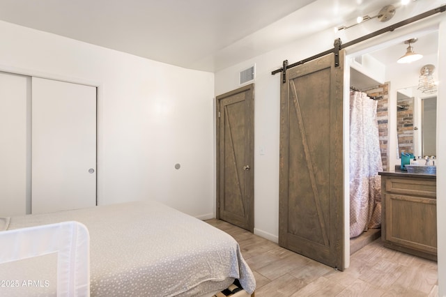 bedroom featuring a barn door, light wood-style flooring, and visible vents