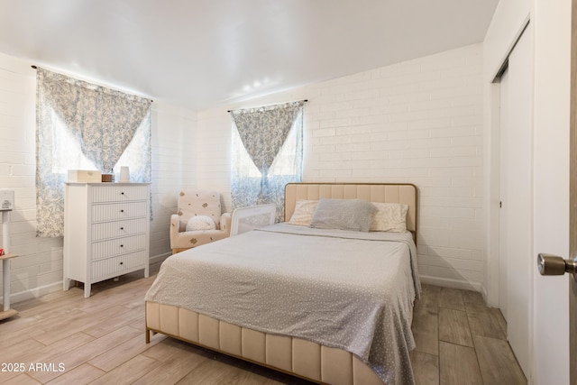 bedroom featuring brick wall and light wood-style flooring