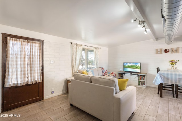 living area with wood finish floors, brick wall, beamed ceiling, and track lighting