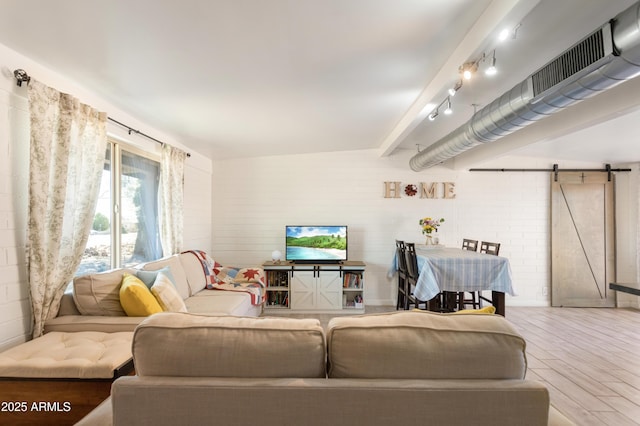 living room with wood finished floors, brick wall, beam ceiling, and a barn door