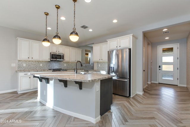 kitchen featuring tasteful backsplash, white cabinetry, a center island with sink, and stainless steel appliances