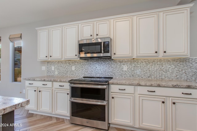 kitchen with light stone countertops, backsplash, stainless steel appliances, and light parquet floors