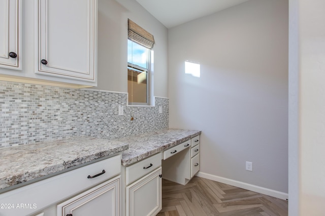 kitchen featuring light stone countertops, built in desk, tasteful backsplash, and white cabinetry